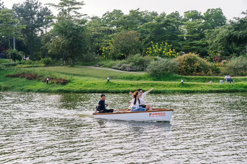 Thuyền nhỏ trên mặt hồ yên ả giữa bãi cỏ và hàng cây trong Flamingo Đại Lải