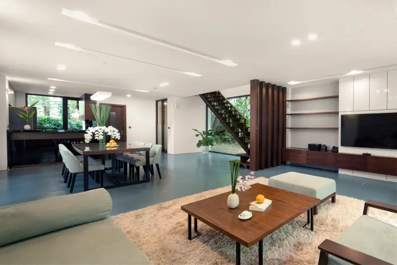 Phòng khách một căn Hilltop Premium Villa: sofa, bàn ăn dài và cầu thang gỗ