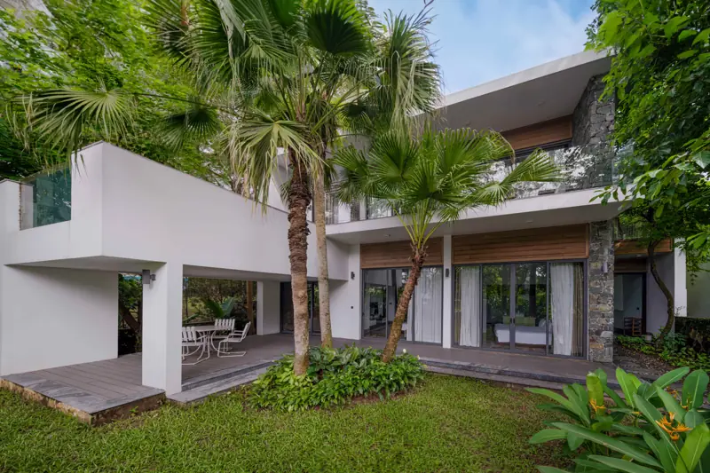 Một căn Kim Tước Villa hai tầng màu trắng, hiên gỗ nhìn ra vườn cọ