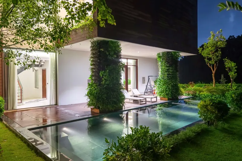 Một căn Lake View Villa lúc chập tối: bể bơi trước hiên, tường cây xanh và đèn vườn