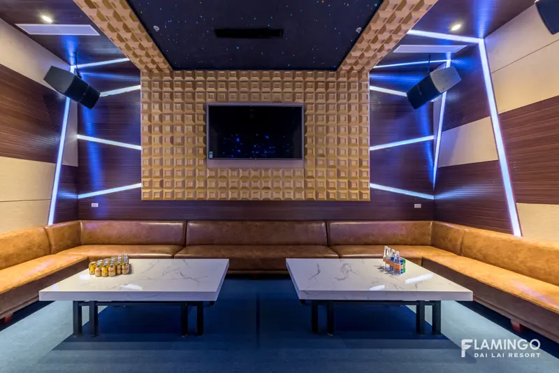 Phòng karaoke rộng với ghế sofa da vòng quanh, hai bàn trắng, màn hình và đèn led xanh