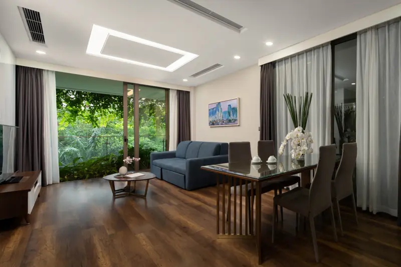 Phòng khách căn Deluxe Sky Residence 2 phòng ngủ: sofa, bàn ăn và cửa kính nhìn ra vườn