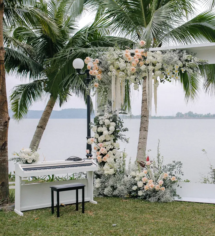 Cổng hoa trắng và đàn piano trắng đặt trên bãi cỏ ven hồ Đại Lải dưới hàng dừa